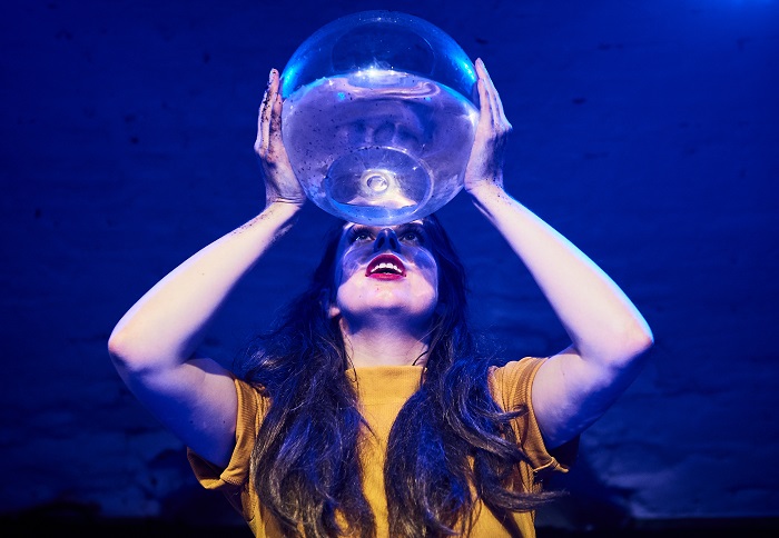 Everything I Didn't Say Alma Tavern And Theatre BristolAn actor holds a large glass bowl filled with water above their head. The back of the set is a rich blue colour