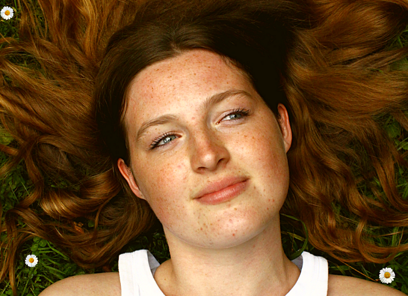 As You Like It Bristol Shakespeare Festival - A young woman lying back on the grass with her hair spread around, looks happily at the sky
