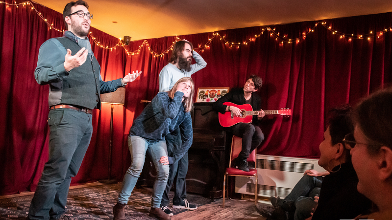 Bristol Improv Theatre - A group of actors on a stage lined by red curtains and draped lights are in full swing of performance